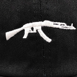 Detailed close-up of white AK-47 rifle embroidery on black cotton baseball cap fabric