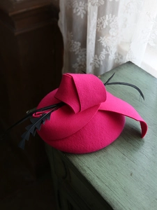 Primer plano de un tocado vintage rosa vibrante con plumas negras sobre una mesa verde.