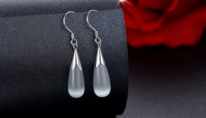 Macro shot of silver teardrop moonstone earrings hanging against a textured grey background