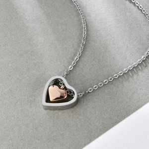 Détail d'un collier en forme de cœur argenté avec un pendentif cœur en or rose