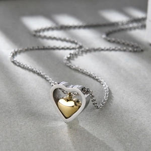 Gros plan détaillé d'un collier cœur évidé en argent avec un petit pendentif cœur doré