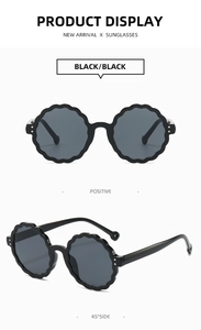Detail of round wavy edge sunglasses in black finish with dark grey lenses