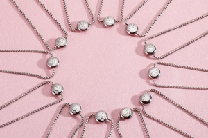 Detail of 12 silver zodiac necklaces with crystal inlays on pink leather background
