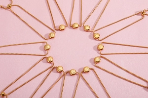 Set of twelve gold adjustable zodiac bracelets arranged in a radial pattern on pink texture