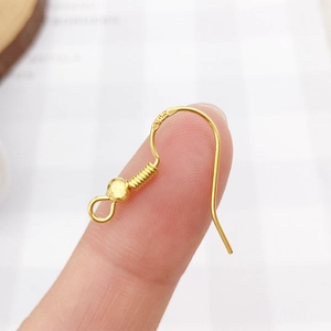 Macro shot of 925 sterling silver ear hooks in gold finish held at fingertips