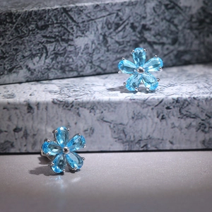 Detail view of flower stud earring with blue zircon stone and silver metal prongs