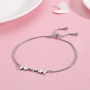 Adjustable stainless steel fish bracelet with heartbeat charm on pink background