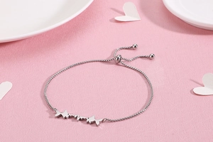 Detail of adjustable silver fish bracelet with heartwave charm on a pink textured background