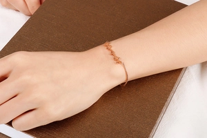 Detail of rose gold butterfly bracelet with hollow wing design on wrist over books