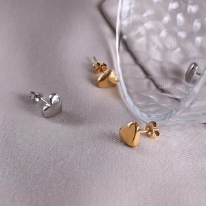 Polished 18k gold and silver titanium steel heart stud earrings on soft purple fabric