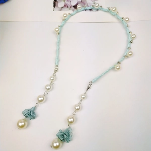 Detail of light blue braided headband with white pearls and fabric flower pendants