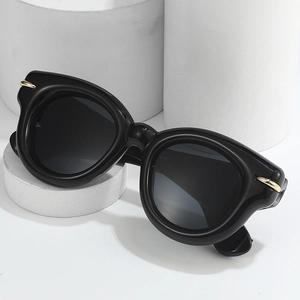Classic oversized black round sunglasses with gold hinge detail on a minimalist stand