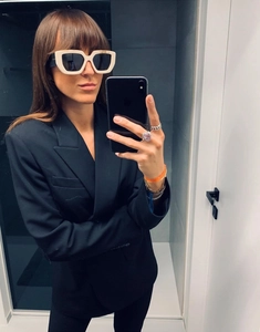 Detail of cream oversized sunglasses with side logo on a person wearing a black blazer