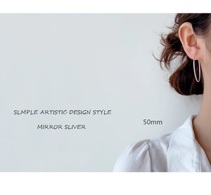 Detail view of large 50mm mirror silver hoop earrings worn on ear in minimalist style