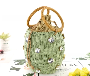 Close-up of green woven straw bucket bag with large rhinestones and drawstring closure