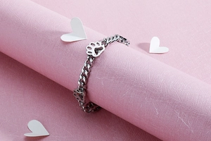 Detail eines silbernen Edelstahlarmbands mit hohlen Pfotenabdrücken auf rosa Papier