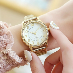 Close-up of elegant gold women watch featuring diamond-studded bezel and woven mesh strap