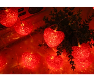 Detail of red heart string lights with crackle texture glowing on green plants
