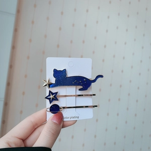 Close-up of three blue enamel hair clips with cat, star, and planet designs