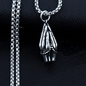 Macro shot of silver stainless steel praying hands pendant on a dark textured surface
