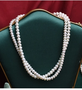 Close-up of double-layer white freshwater pearl necklace on dark green vintage frame