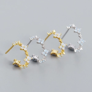 Detail of gold and silver C-shaped hoop earrings with milky stone clover floral patterns
