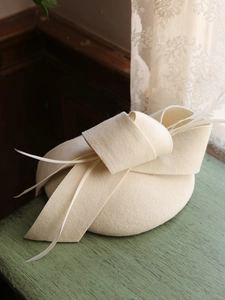 Elegante tocado de fieltro de lana blanco roto con detalle de plumas y lazo decorativo