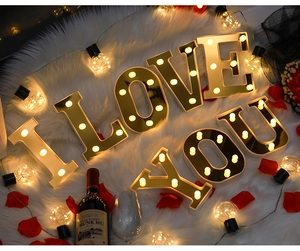 Golden LED I LOVE YOU letter lights with warm bulbs on white rug and rose petals