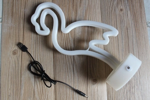 Close-up of white flamingo neon lamp with round base and USB power cable on wood surface
