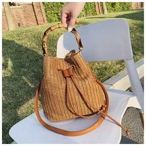 Detail of a straw bucket bag featuring a bamboo handle and brown leather drawstring closure