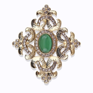 Dettaglio di spilla dorata vintage con smeraldo verde e strass trasparenti brillanti