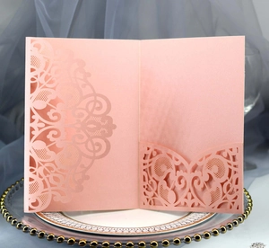 Close-up of pink laser-cut lace invitation card on gold beaded plate with tulle background