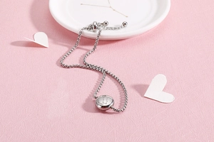 Macro shot of silver zodiac bracelet with Gemini engraved pendant on pink background