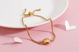 Adjustable gold Scorpio zodiac bracelet with engraved disc and crystal on pink background