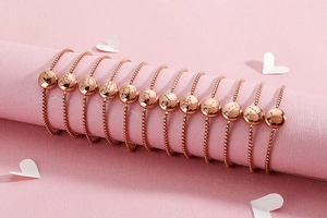 Rose gold zodiac bracelets with diamonds displayed on a pink textured background