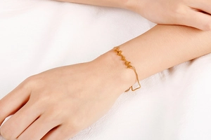 Detail of a minimalist gold butterfly bracelet on a woman wrist with five charms