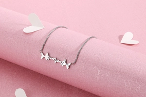 Close-up of stainless steel fish pendant with heart rhythm line on pink background