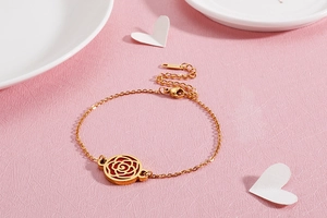 Détail d'un bracelet doré avec un pendentif rose rouge ajouré au motif floral élégant