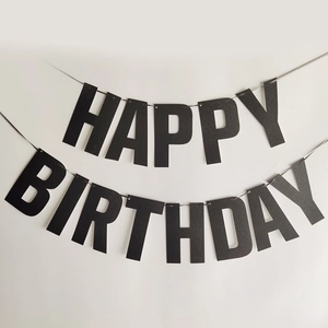 Glittery black Happy Birthday banner hanging against a white wall for party decor