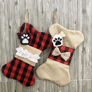 Linen and red plaid dog bone Christmas stockings with paw tags on gray wood wall