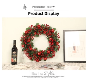 Christmas wreath with green holly leaves, red berries, and ornaments on a white wall