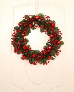 Close-up of artificial Christmas wreath with green holly leaves and red berries on white door