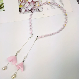 Detailed macro view of pink fabric ribbon chain with pearls and floral pendant