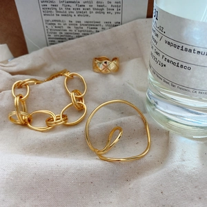 Detail view of gold lattice ring and chain bracelet on a minimalist fabric background