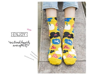 Detail shot of yellow cotton crew socks featuring colorful floral patterns on a stone background