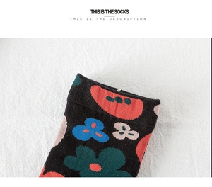 Close-up of black cotton crew socks featuring colorful floral knit patterns and ribbed cuffs
