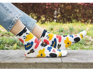 Detailed view of white cotton mid-calf socks with vibrant floral patterns on stone steps