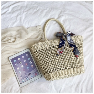 Detail of woven straw handbag with decorative silk scarf next to a tablet for size scale