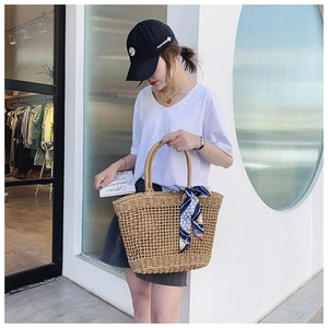 Detail of woven straw tote bag with blue polka dot silk scarf handle in outdoor setting