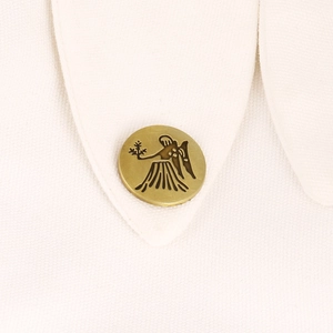 Close-up of vintage bronze zodiac brooch with Virgo motif on a white fabric collar